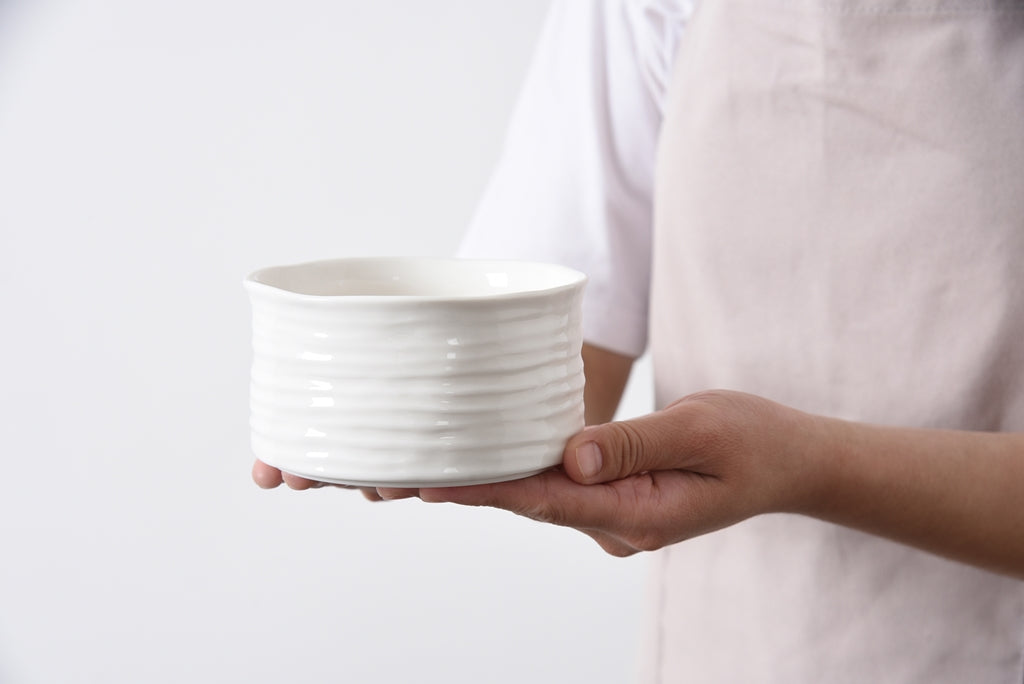 Person holding a white ceramic bowl against a plain background