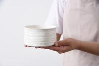 Person holding a white ceramic bowl against a plain background
