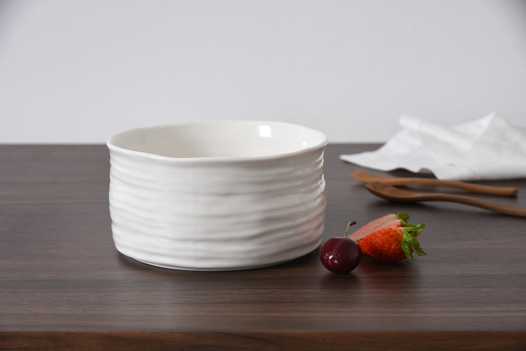White ceramic bowl on a wooden surface with strawberries and a napkin.