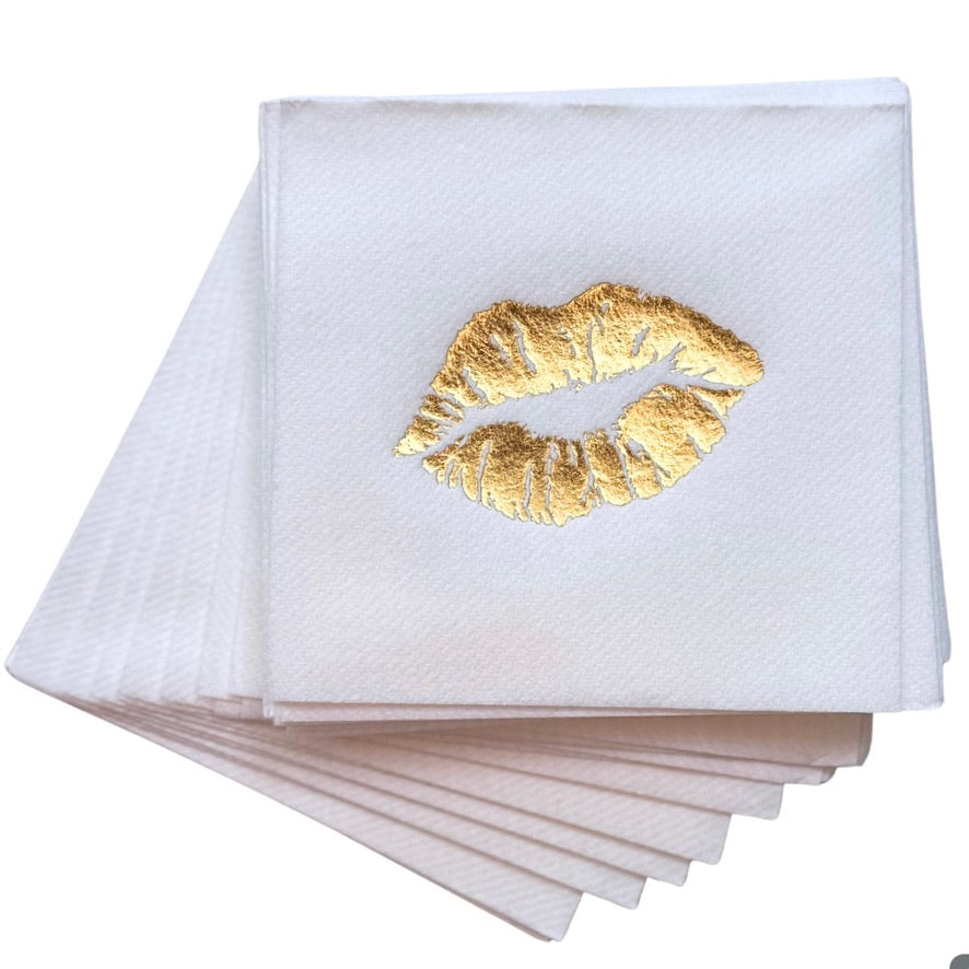 A stack of white paper napkins with a metallic gold foil lip print on the top napkin, set against a plain white background.