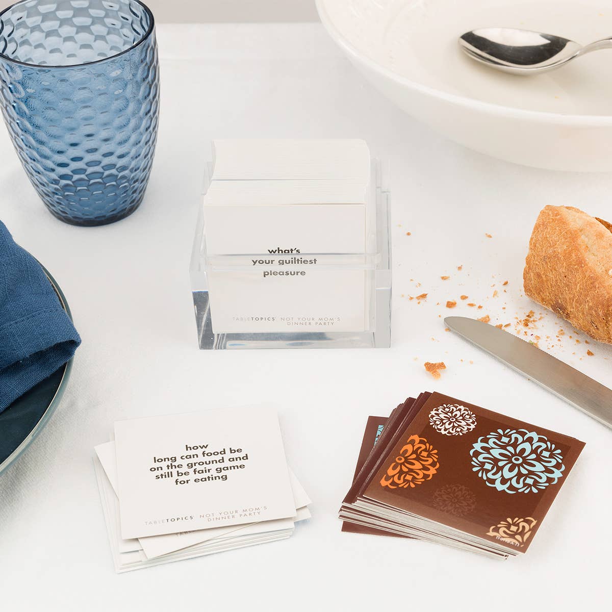 Table setting with cards, a blue glass, and bread on a white surface