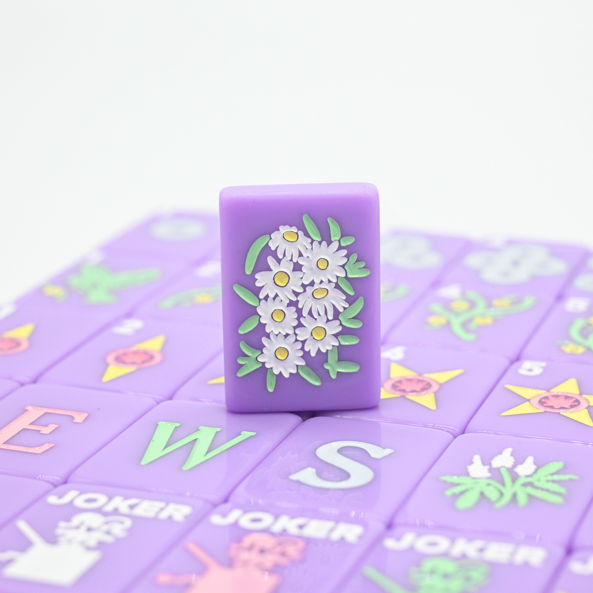 Purple mahjong game piece with floral design on a purple game board with letter tiles.