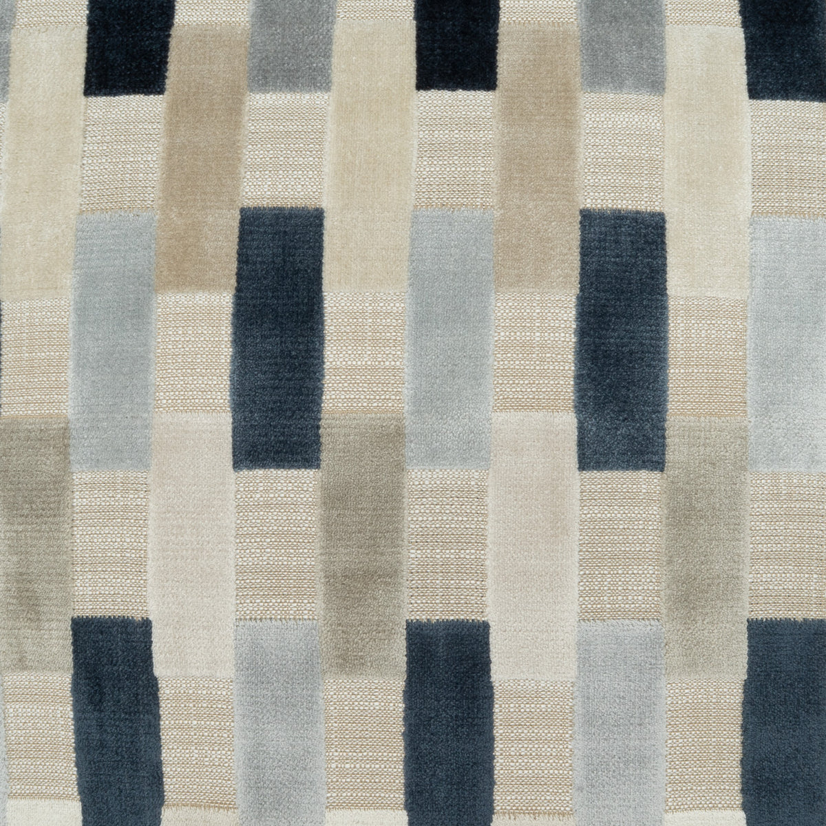 A close-up of a woven textile with a geometric patchwork pattern in beige, cream, light gray, and dark navy blue blocks.