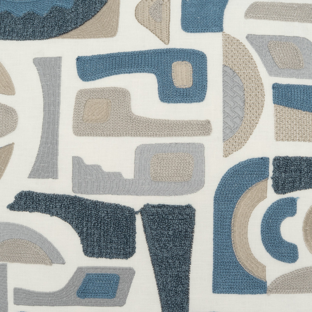 A close-up of a textured fabric or wallpaper featuring an abstract mid-century modern pattern with geometric shapes in slate blue, charcoal gray, and beige on an off-white background.