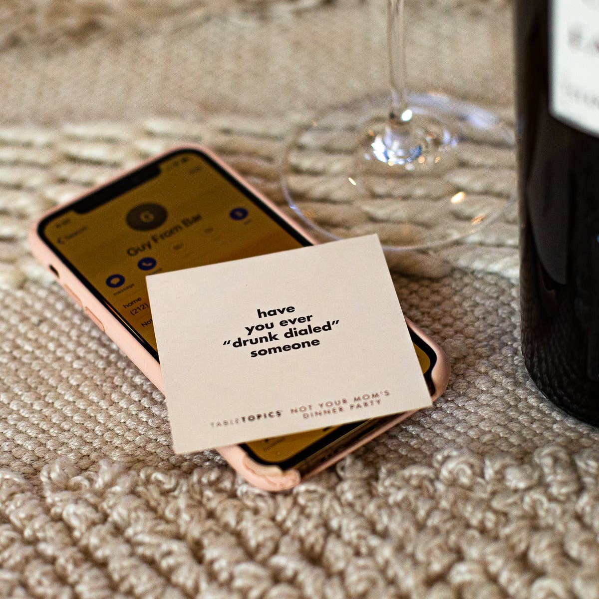 Phone with a card on a textured surface next to a glass and bottle