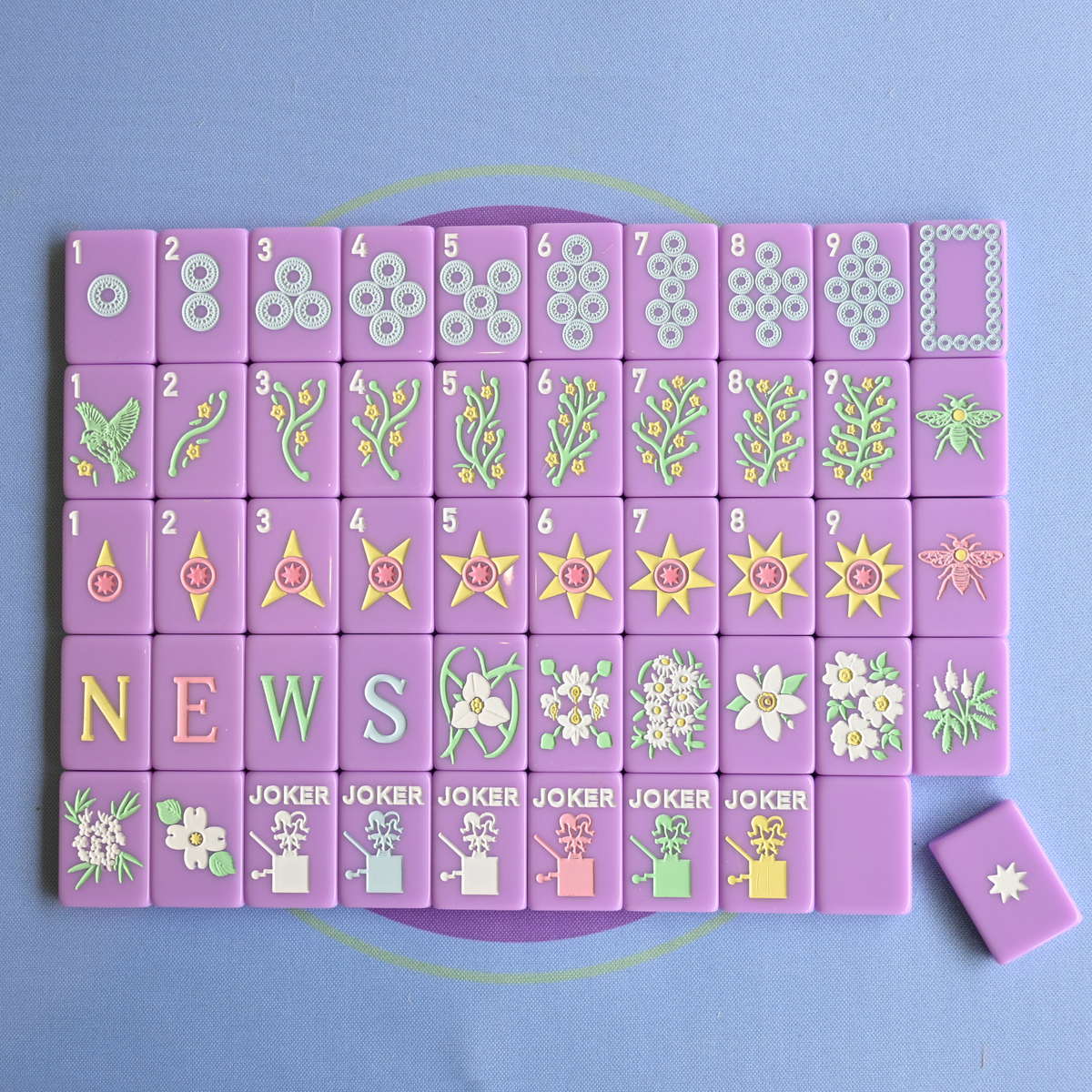 Set of purple mahjong tiles with floral and geometric designs on a blue background