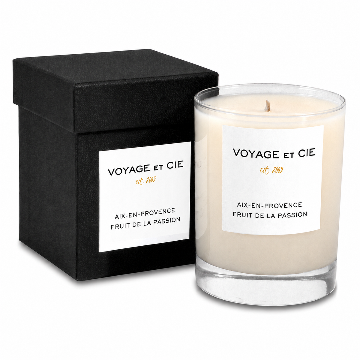 A glass jar candle with cream-colored wax and a white label reading 'VOYAGE et CIE est. 2013 BALI GARDENIA' stands next to its black square box, which has a matching white label.