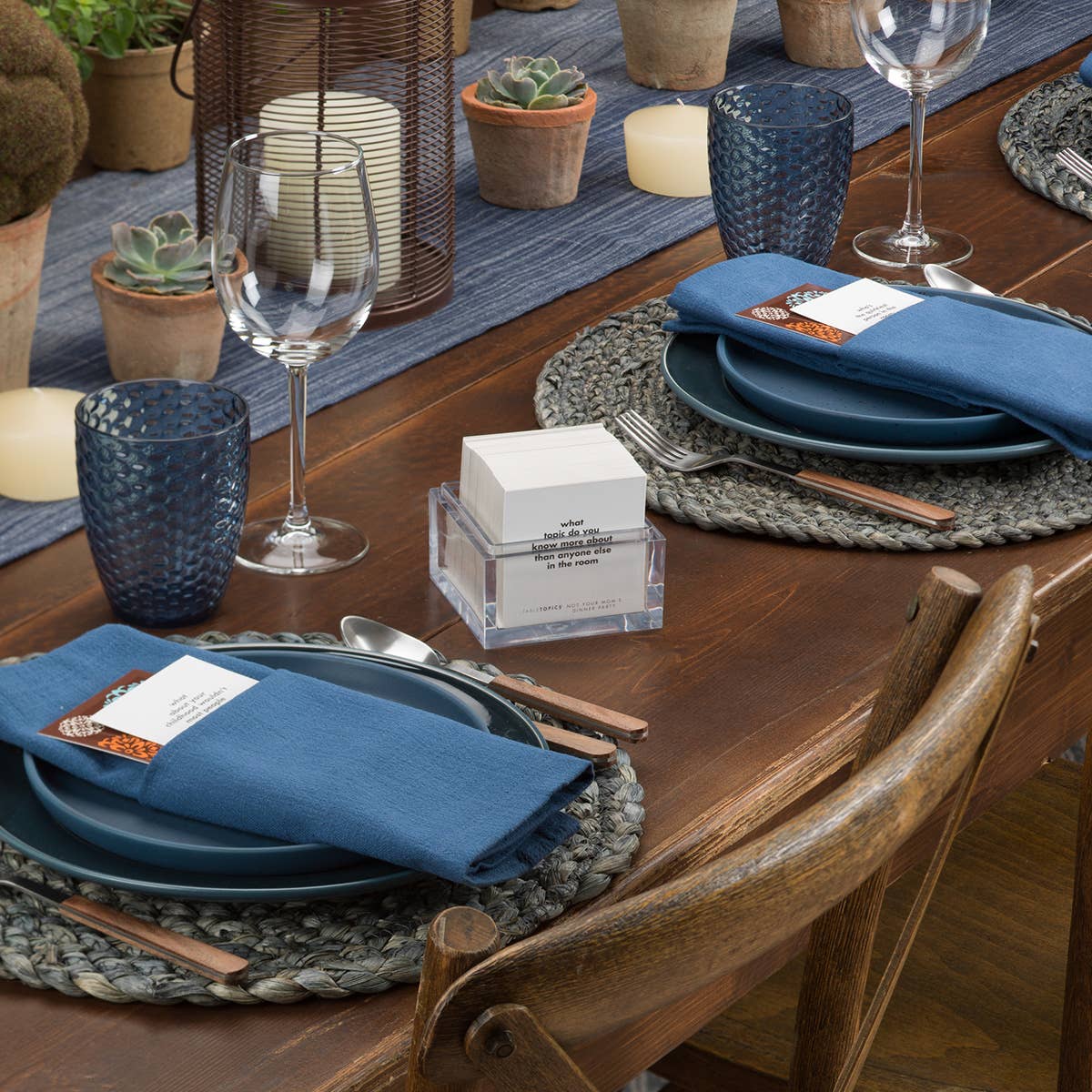 Dining table set with blue plates, napkins, and glasses on a wooden table.