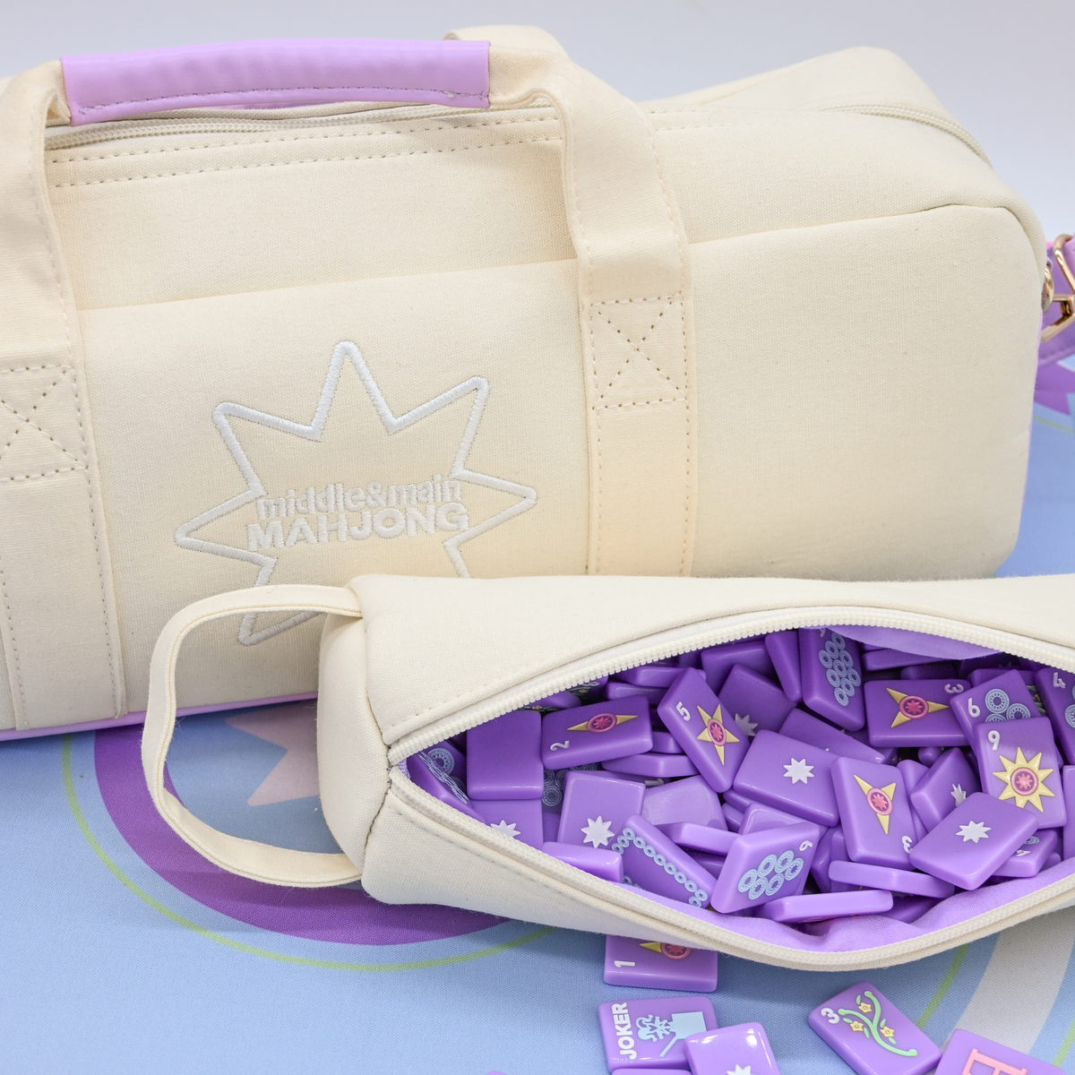 Beige duffel bag with purple mahjong tiles containing purple game pieces on a matching purple background.