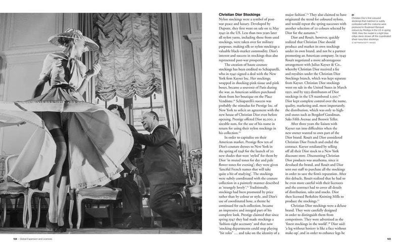 Black and white scene of a woman in a large dress with a hat, sitting at a table with a man, Christian Dior in an elegant room.