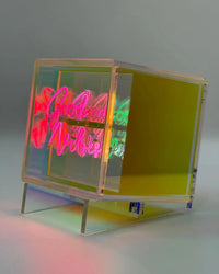 Neon sign with 'Good Vibes' on a stand against a gray background