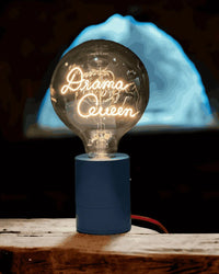Decorative light bulb with 'Drama Queen' text on a wooden surface with a dark background