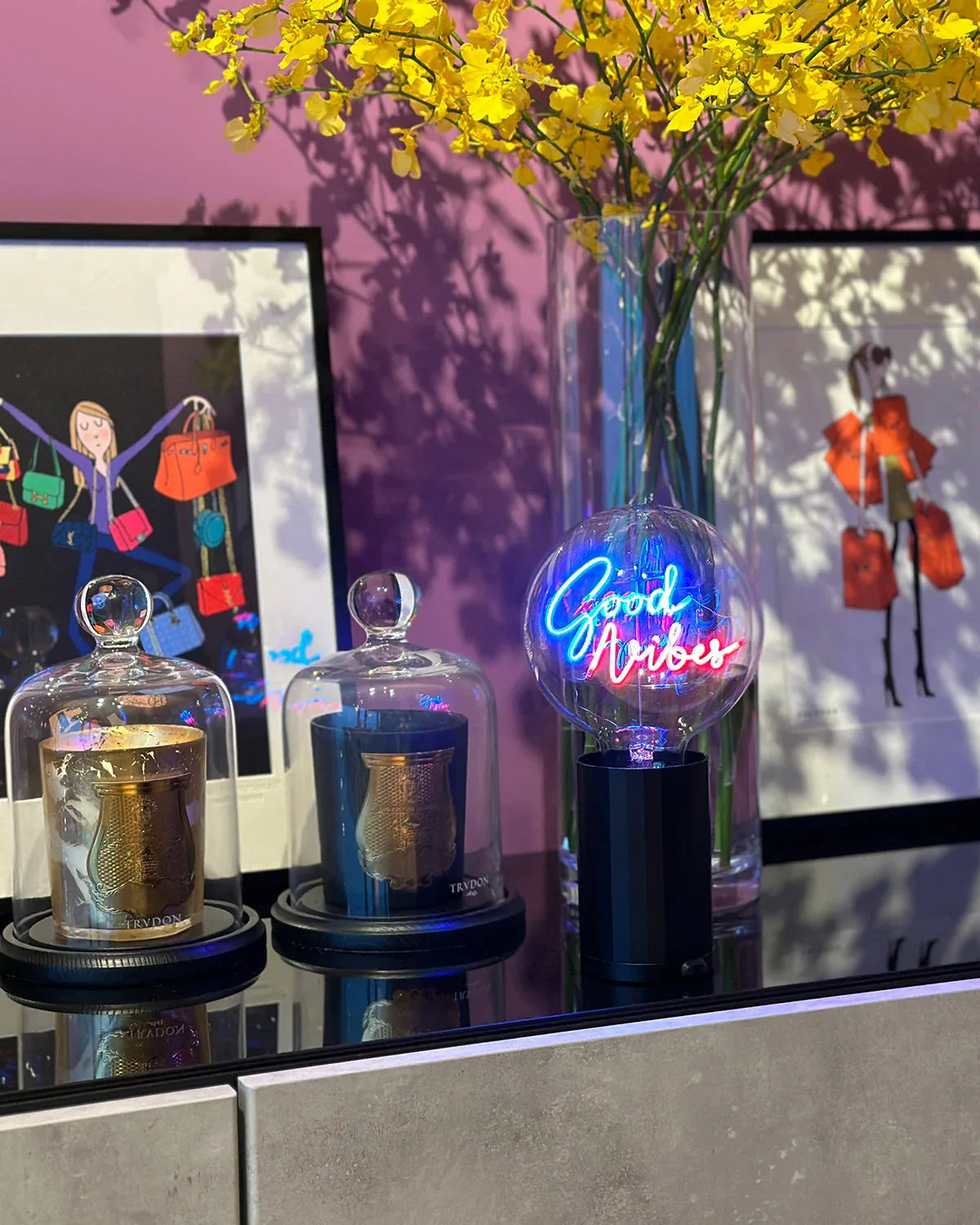 Decorative items on a table with 'Good Vibes' neon sign, flowers, and artwork in the background.