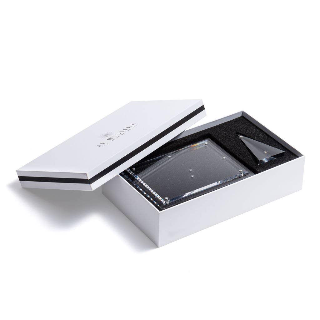 Open white box with a clear lid containing a Hand-cut beveled acrylic picture frame with a magnetic pyramid stand on a white background