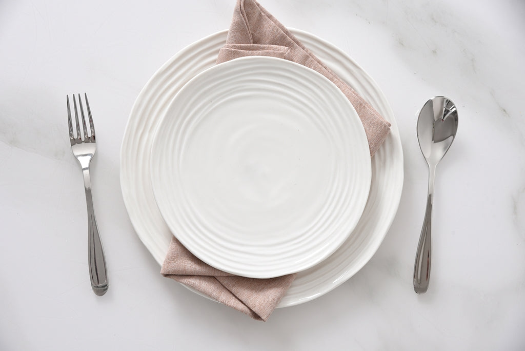 White ceramic plate with a pink napkin, fork, and spoon on a light gray background
