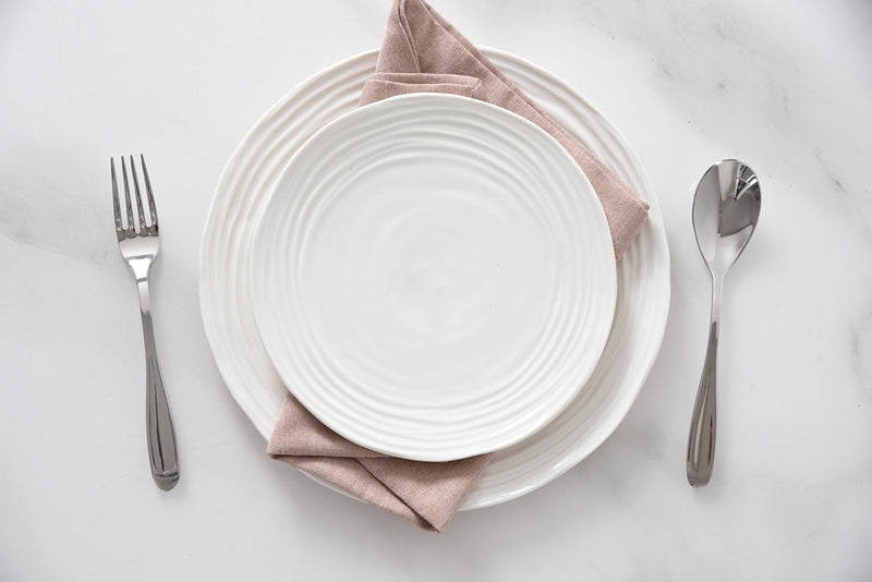 White ceramic plate with a pink napkin, fork, and spoon on a light gray background