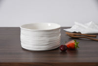 White ceramic bowl on a wooden surface with strawberries and a napkin.