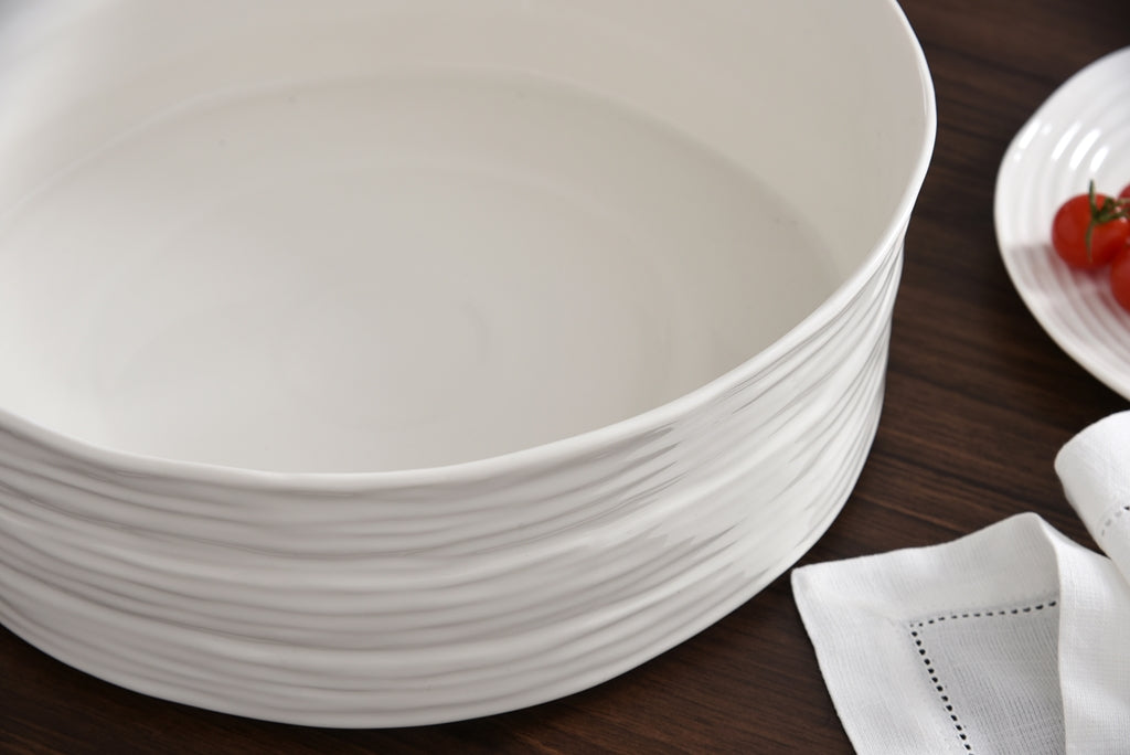 Stack of white ceramic plates on a wooden surface with a white napkin and small dish with tomatoes.