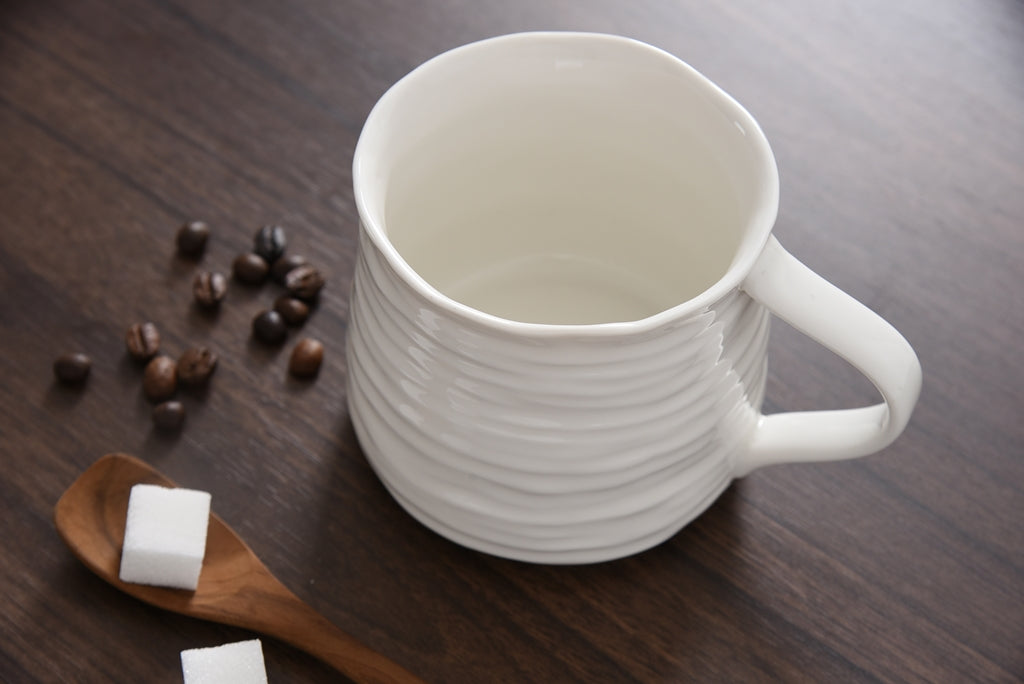 White ceramic mug on a wooden surface with coffee beans and sugar cubes.