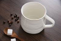 White ceramic mug on a wooden surface with coffee beans and sugar cubes.