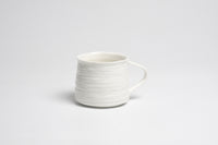 White ceramic mug with a textured design on a light gray background