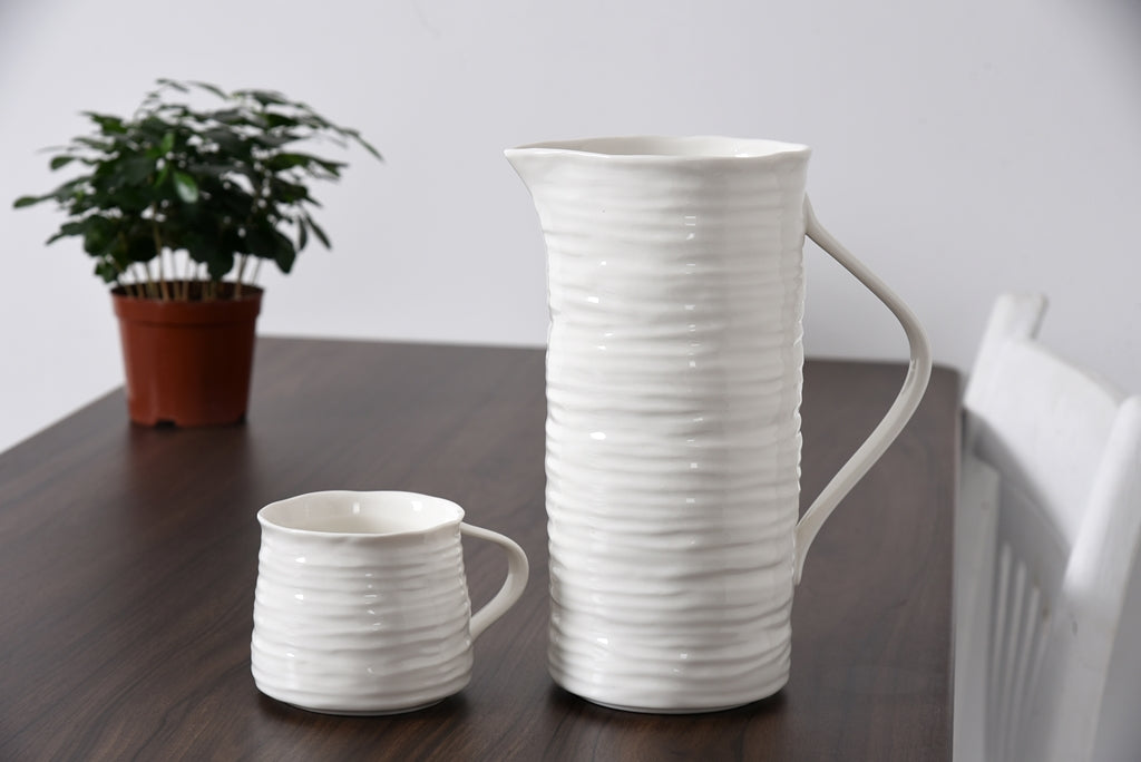 White ceramic pitcher and mug on a wooden table with a plant in the background
