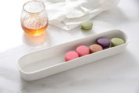 Colorful macarons in a white tray on a marble surface with a glass of orange juice.