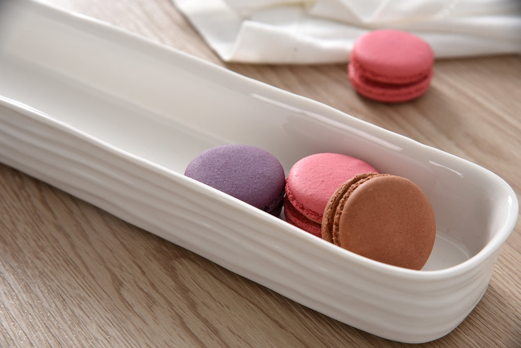 Colorful macarons in a white ceramic tray on a wooden surface