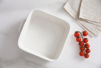White square bowl on a light surface with cherry tomatoes and a folded beige cloth.