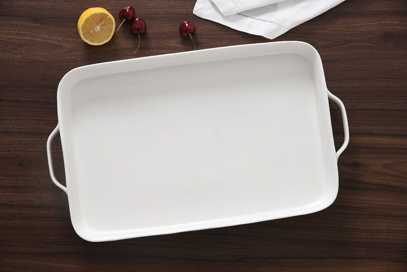 White ceramic baking dish on a wooden surface with a lemon and cherries.
