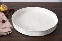 Stack of white ceramic plates on a wooden surface with a lemon and cherries.