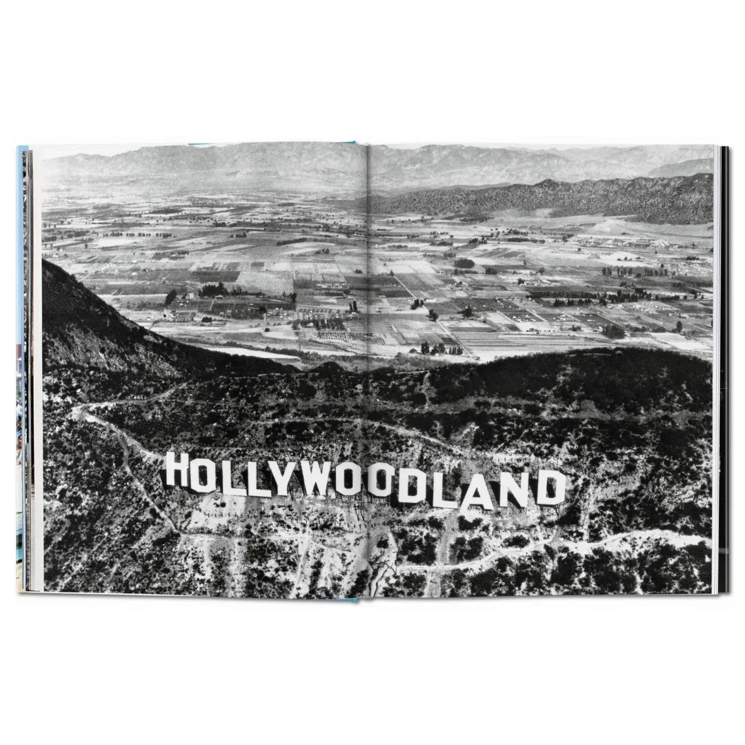 Black and white aerial view of a sign reading 'Hollywoodland' with mountains in the background.