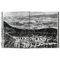 Black and white aerial view of a sign reading 'Hollywoodland' with mountains in the background.