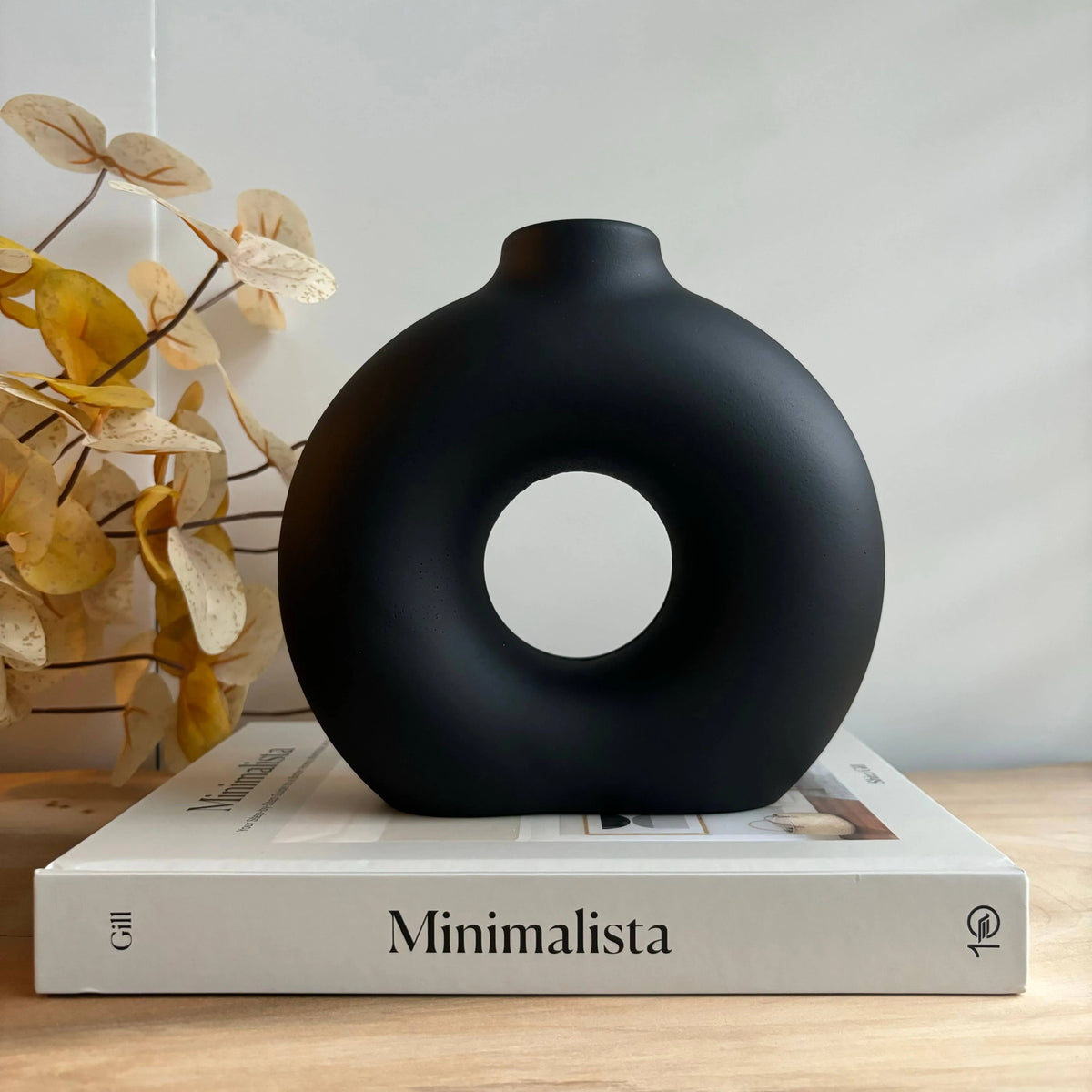 Marble Halo Vase Matt Black Decorative Vase with circular design on a book titled 'Minimalista' with decorative leaves in the background.