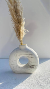 Marble-patterned vase with a circular hole containing dried pampas grass on a light background
