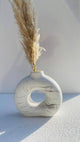 Marble-patterned vase with a circular hole containing dried pampas grass on a light background