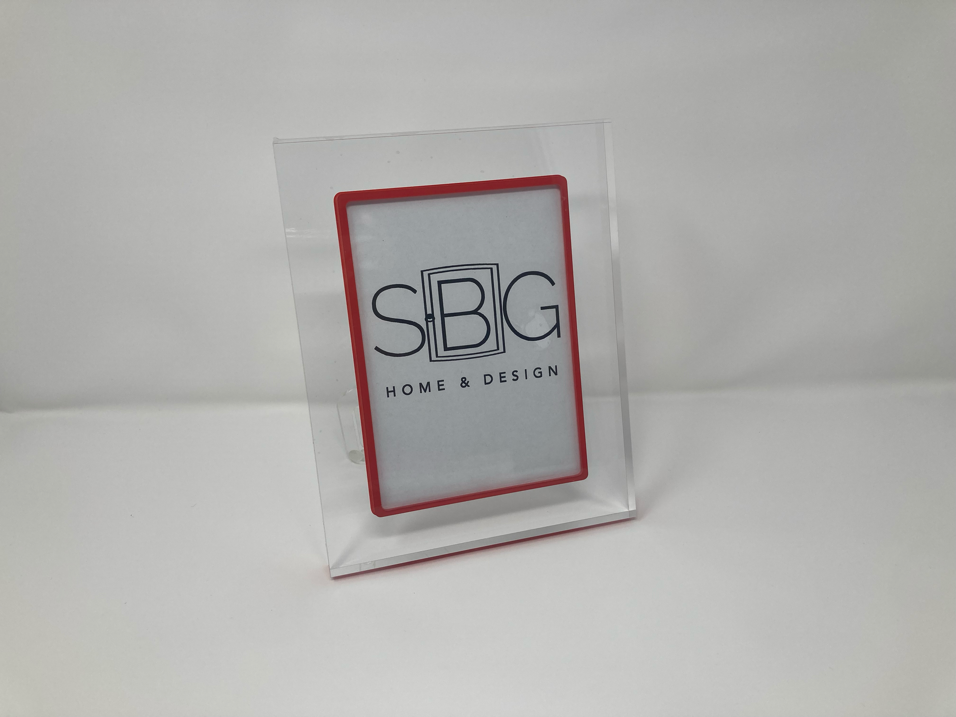 Clear plastic photo frame with red border and 'SIBG Home & Design' logo on a white background