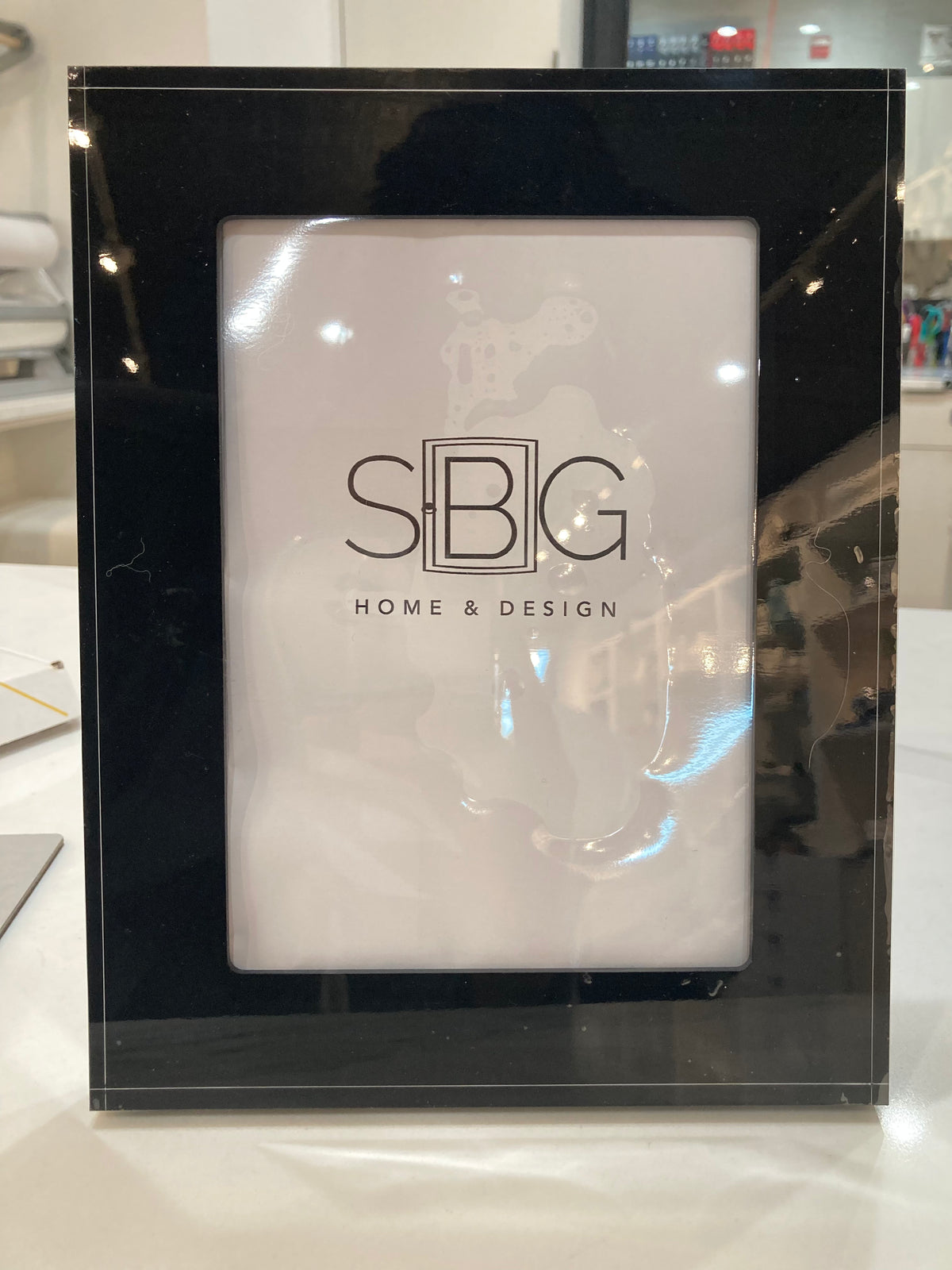 Black picture frame with SBG Home & Design logo on a white surface