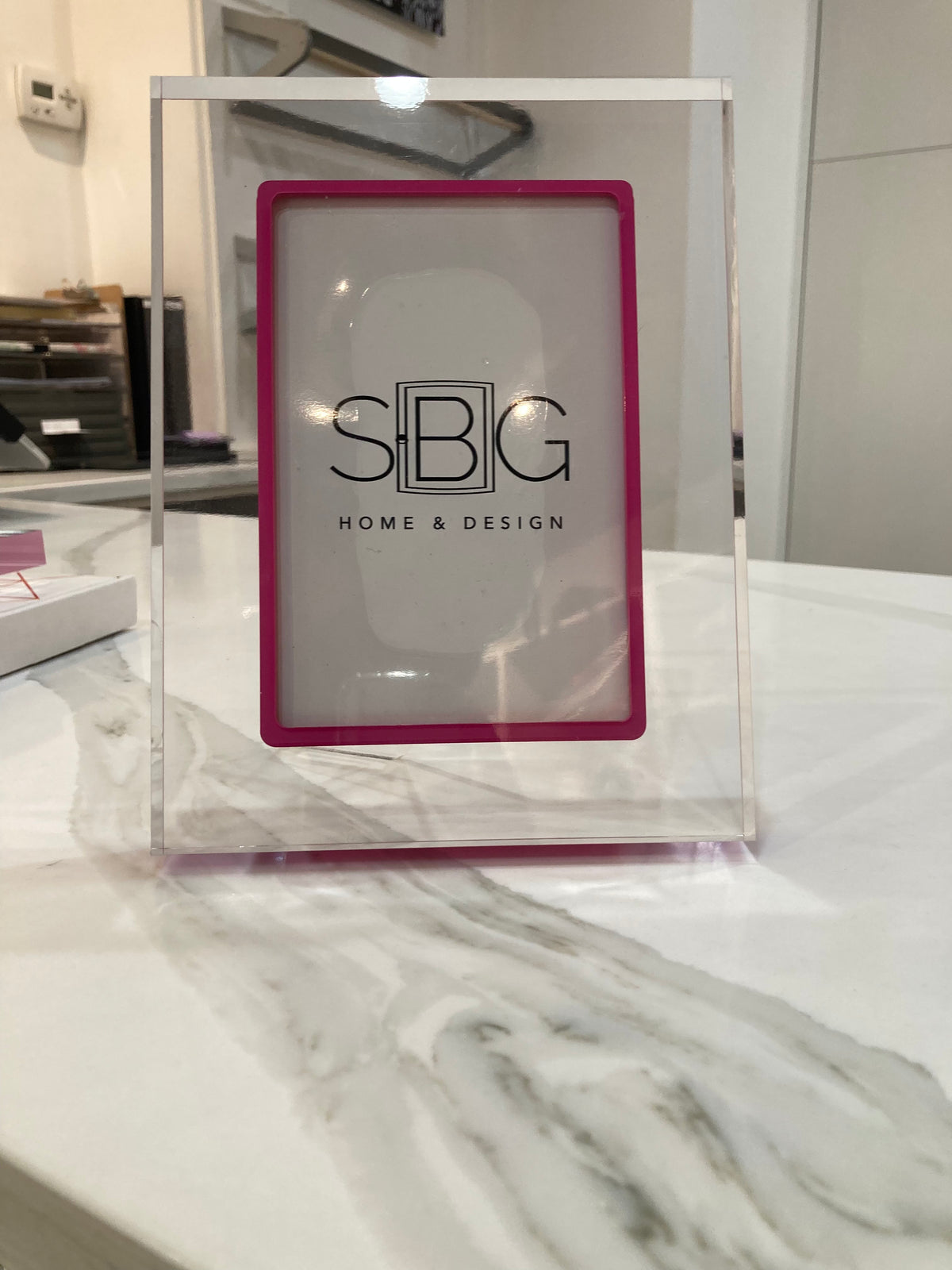 Exuberant Pink Acrylic frame with SBG Home & Design logo on a marble surface