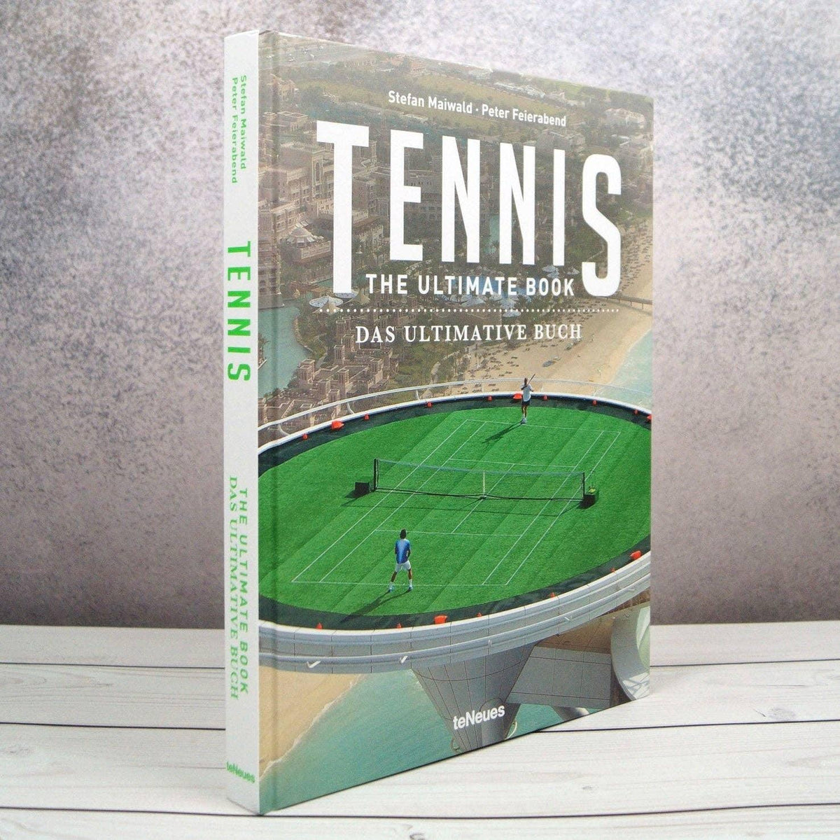 Book titled 'Tennis: The Ultimate Book' on a wooden surface with a gray background