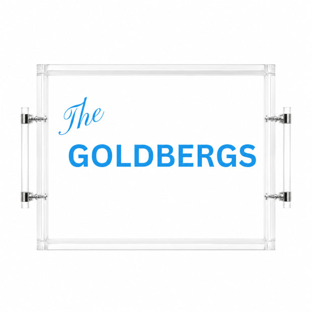 Clear acrylic serving tray with a white insert and blue printed text reading 'The GOLDBERGS', shown on a white background with metal side handles.