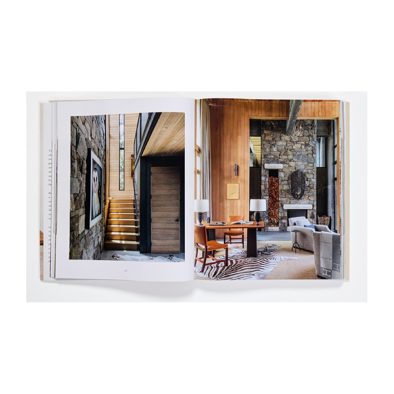 An open architectural photography book displayed against a clean white background, showing two interior design pages with wood paneling, stone walls, stairs, and a dining area.