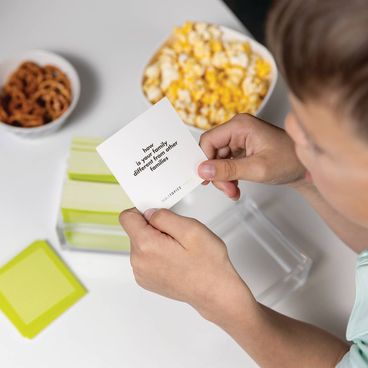 Child holding a card with a question about family differences, with snacks in the background