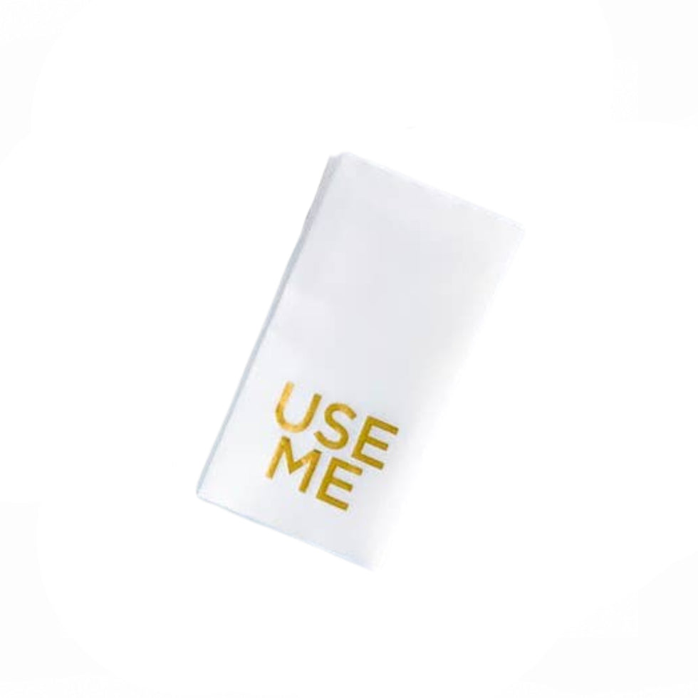 A white rectangular napkins with the words 'USE ME' printed in gold foil on the front, shown on a plain white background.