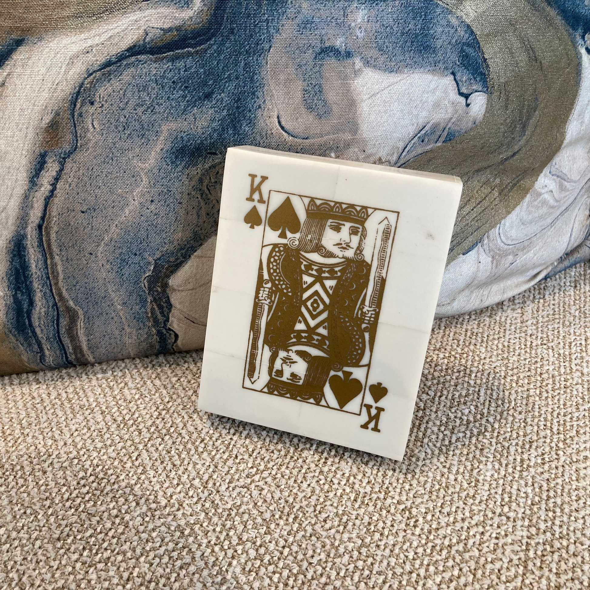 King of Spades playing card on a textured surface with a marbled pillow in the background