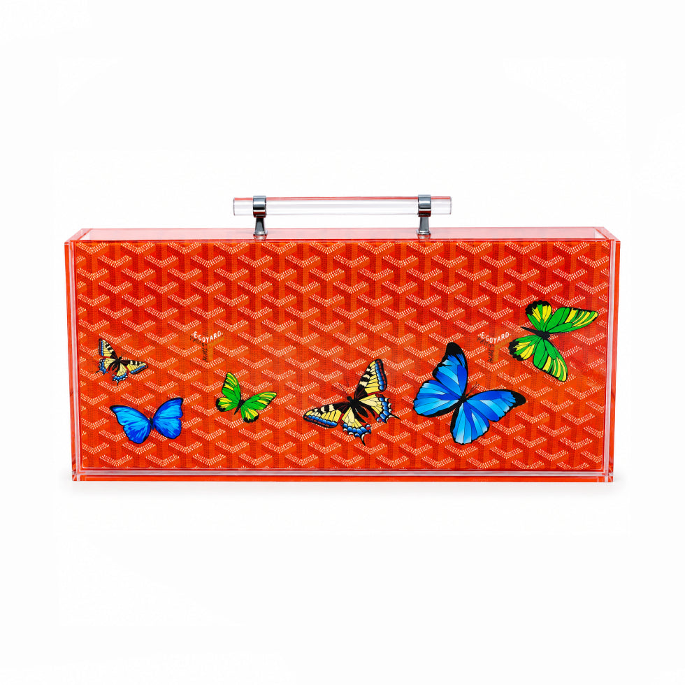 A rectangular Goyard handbag in translucent orange-red acrylic with the brand's signature chevron pattern and colorful butterfly illustrations, featuring a clear top handle.