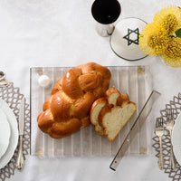 Striped challah board smoke with knife and challah bread on top.