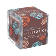 A clear acrylic cube-shaped box for Tabletopics dinner party questions, featuring a dark brown printed cover with orange and blue floral patterns and white text.
