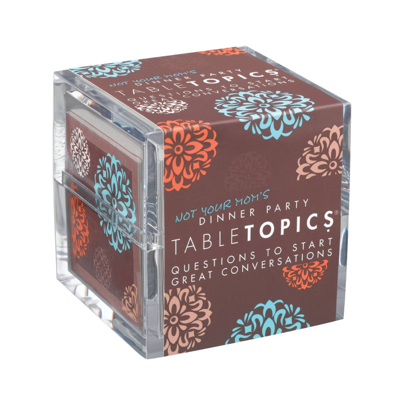 A clear acrylic cube-shaped box for Tabletopics dinner party questions, featuring a dark brown printed cover with orange and blue floral patterns and white text.
